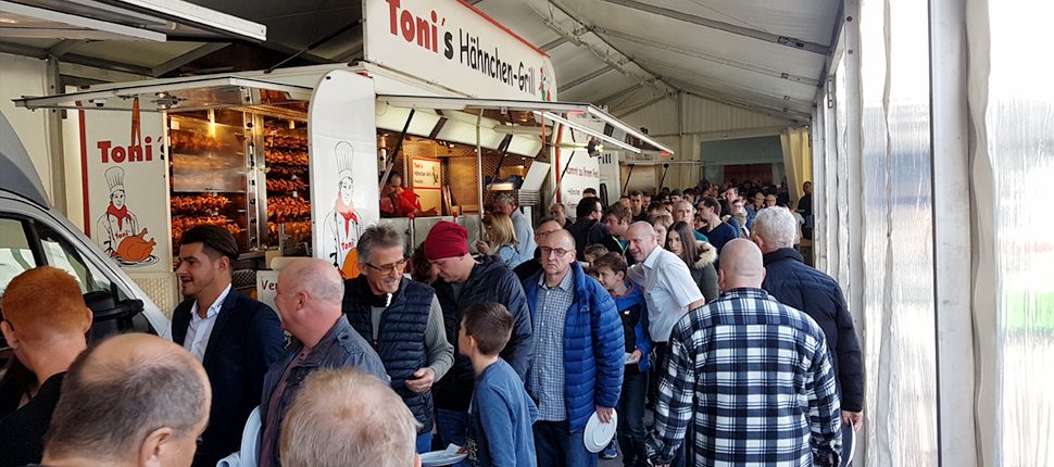 Gäste stehen im Festzelt vor dem geöffneten Grillwagen an